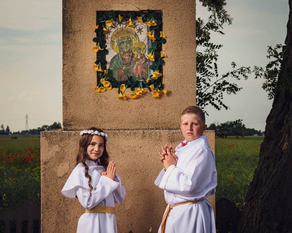 Pamiątka pierwszej komunii świętej - zdjęcie przy wiejskiej przydrożnej kapliczce.